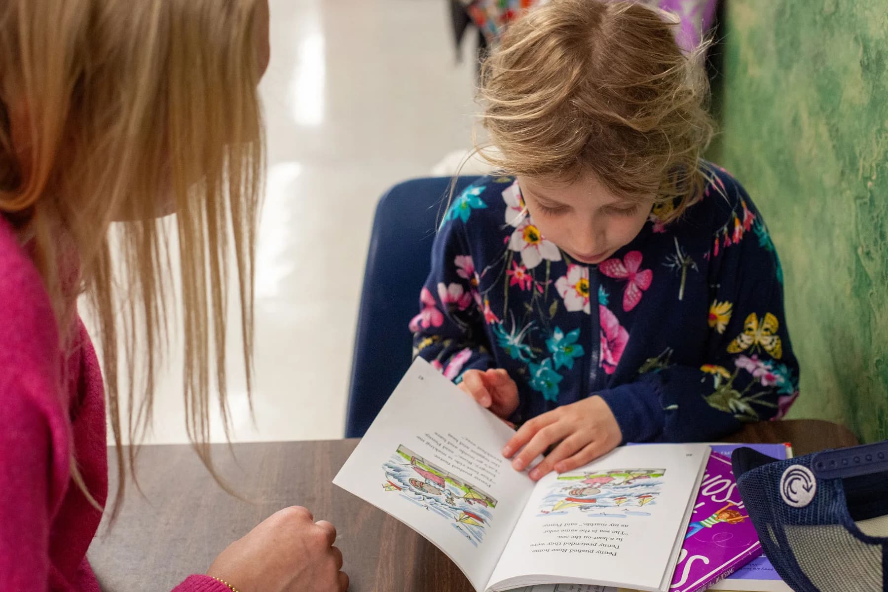 A student reading a book with a volunteer